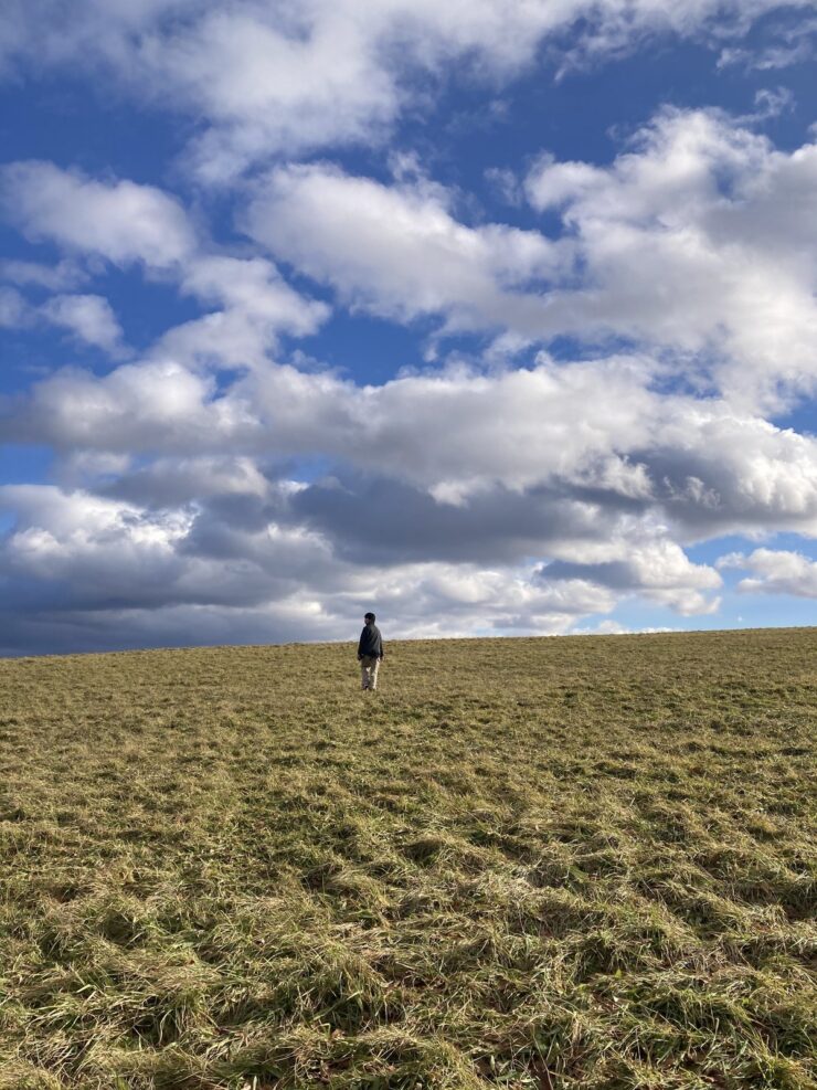 北海道の草原を歩く在校生の後ろ姿。広い空と雲