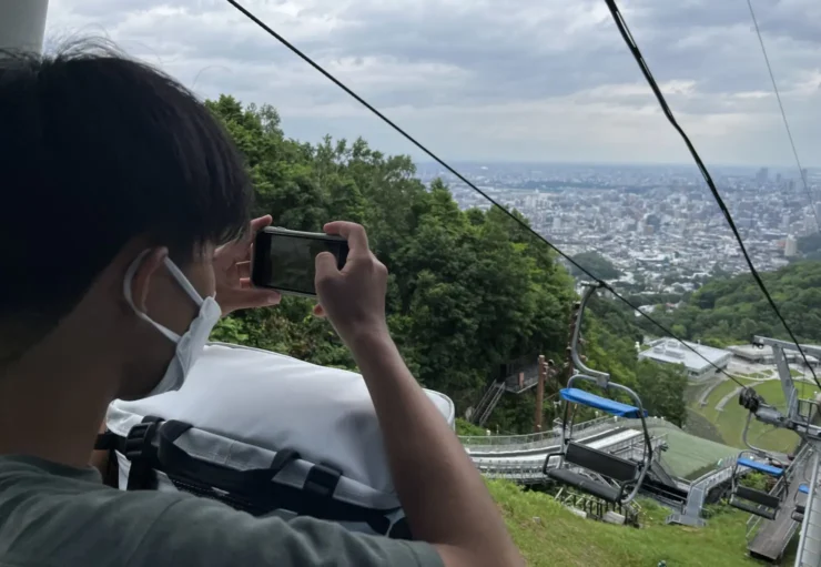 札幌のリフトから、眼下に広がる市街地をスマートフォンで撮る在校生の後ろ姿
