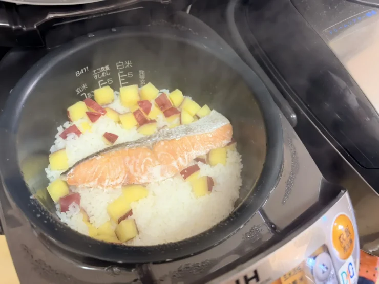 炊飯器の中で、さつまいもと切り身の鮭をのせて炊きあがったご飯